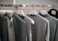 A clothing rack displaying a selection of gray and black knitwear, including sweaters and cardigans, hung on white hangers. The garments feature various textures and styles, creating a cozy and elegant display.