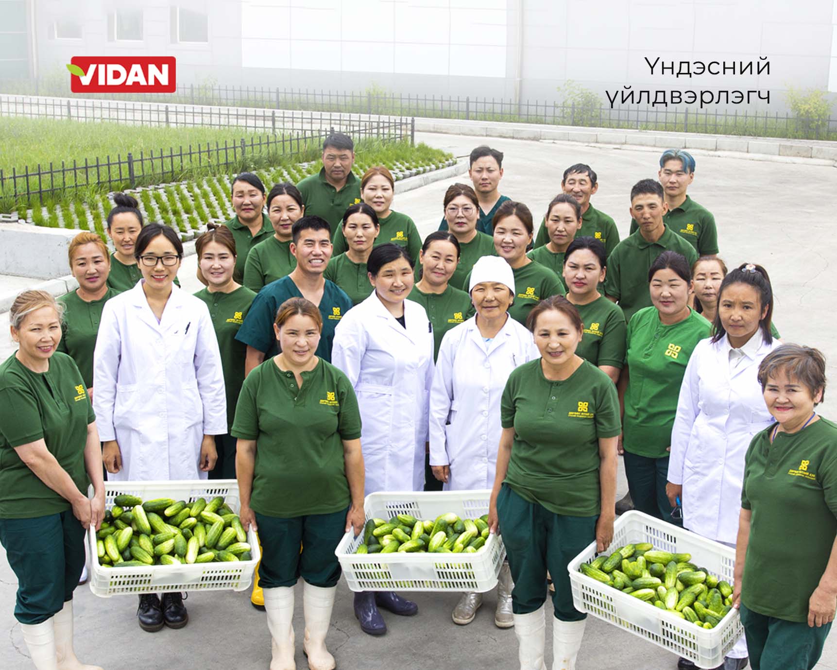 A group of people wearing green uniforms stand outdoors, holding trays of vegetables. Some are dressed in white lab coats. A building and garden are visible in the background. Text in a foreign script is present in the image.