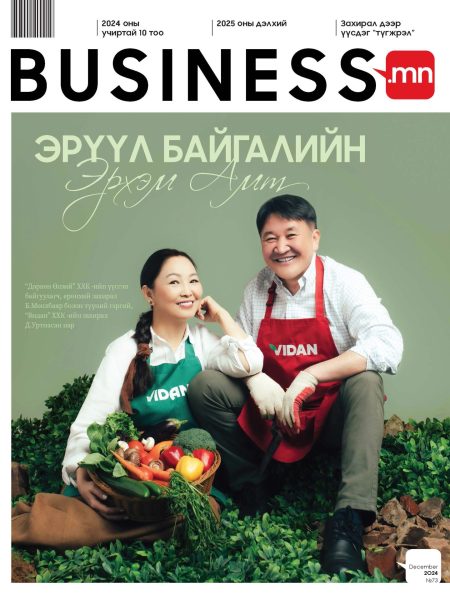 A smiling man and woman sit on a pile of rocks, both wearing aprons. The woman holds a basket filled with vegetables. The magazine cover features text in a non-English script with a "Business.mn" logo at the top.