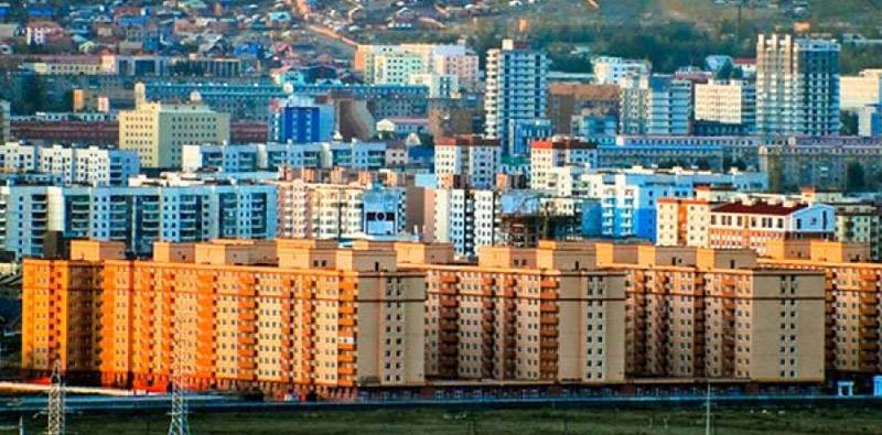 A cityscape featuring rows of colorful apartment buildings, with a variety of architectural styles. The foreground shows large, rectangular buildings in warm hues, while the background offers a mix of high-rise structures against a hilly backdrop.