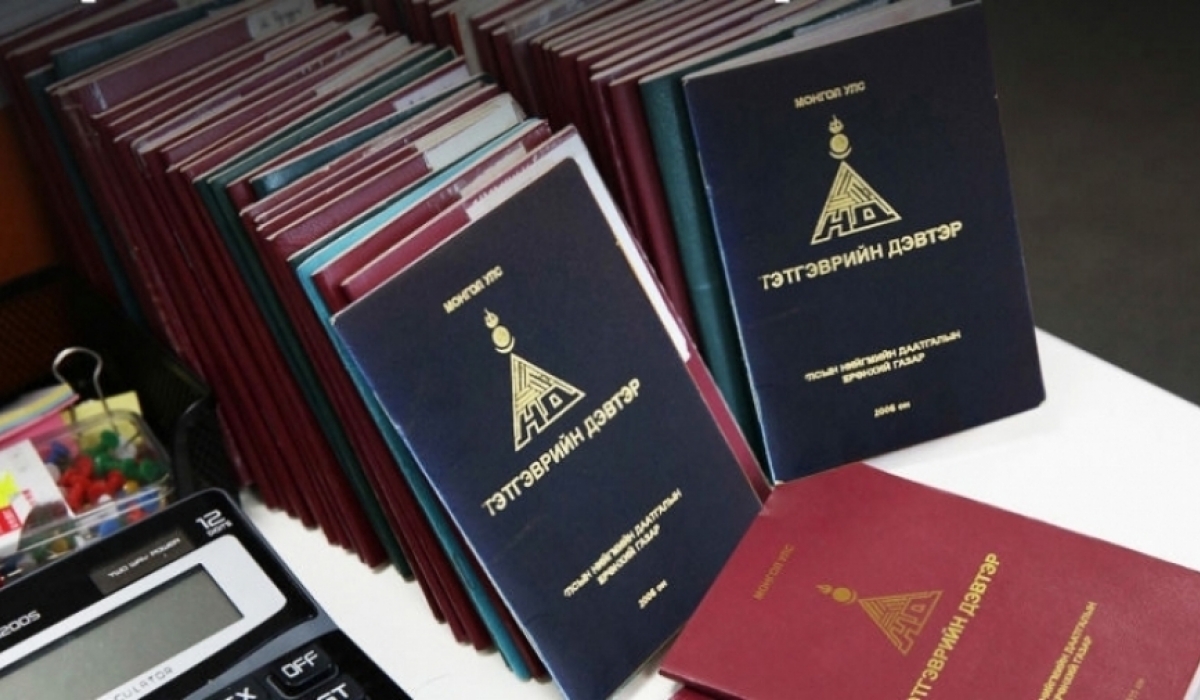 A stack of open and closed booklets on a table with text in a foreign script on the covers. A calculator is partially visible in the foreground. The booklets are predominantly red and blue.