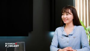 A person with long dark hair, smiling and wearing a light blue jacket, sits at a table in a studio setting, ready to discuss "Хүний нөөцийн хомсдлыг хэрхэн шийдэх вэ? (№291)." A "Business Podcast" logo is visible in the corner.