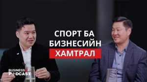 Two men are sitting and smiling in an interview setting with text in a foreign language on the screen. The background is dark, and a podcast logo is visible in the corner.