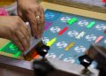 Close-up of hands using a squeegee to spread colorful inks over a screen printing frame with various paint streaks and circular logos.