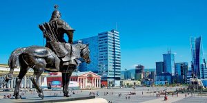 A large bronze statue of a warrior on horseback, symbolizing growth and change, overlooks a busy city plaza. Modern skyscrapers and a historic building surround the square, with people walking below. The clear blue sky suggests it’s the perfect time for transformative opportunities.