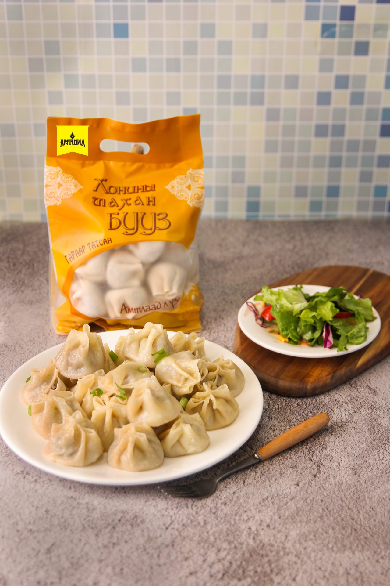 Plate of dumplings garnished with herbs, next to a small side salad on a wooden board. There is a yellow packet of dumplings in the background against a tiled wall.