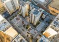 Aerial view of a modern residential complex with tall apartment buildings and landscaped courtyards, ideal for those seeking ипотекийн зээл. Several playgrounds, parking areas, and paths are visible between the buildings, while nearby roads and construction sites can be seen in the background.