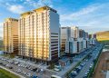 Aerial view of modern high-rise apartment buildings, potential investments for ипотекийн зээл, illuminated by the setting sun. The scene includes a busy street with parked cars, a green landscape in the background, and a blue sky with scattered clouds.