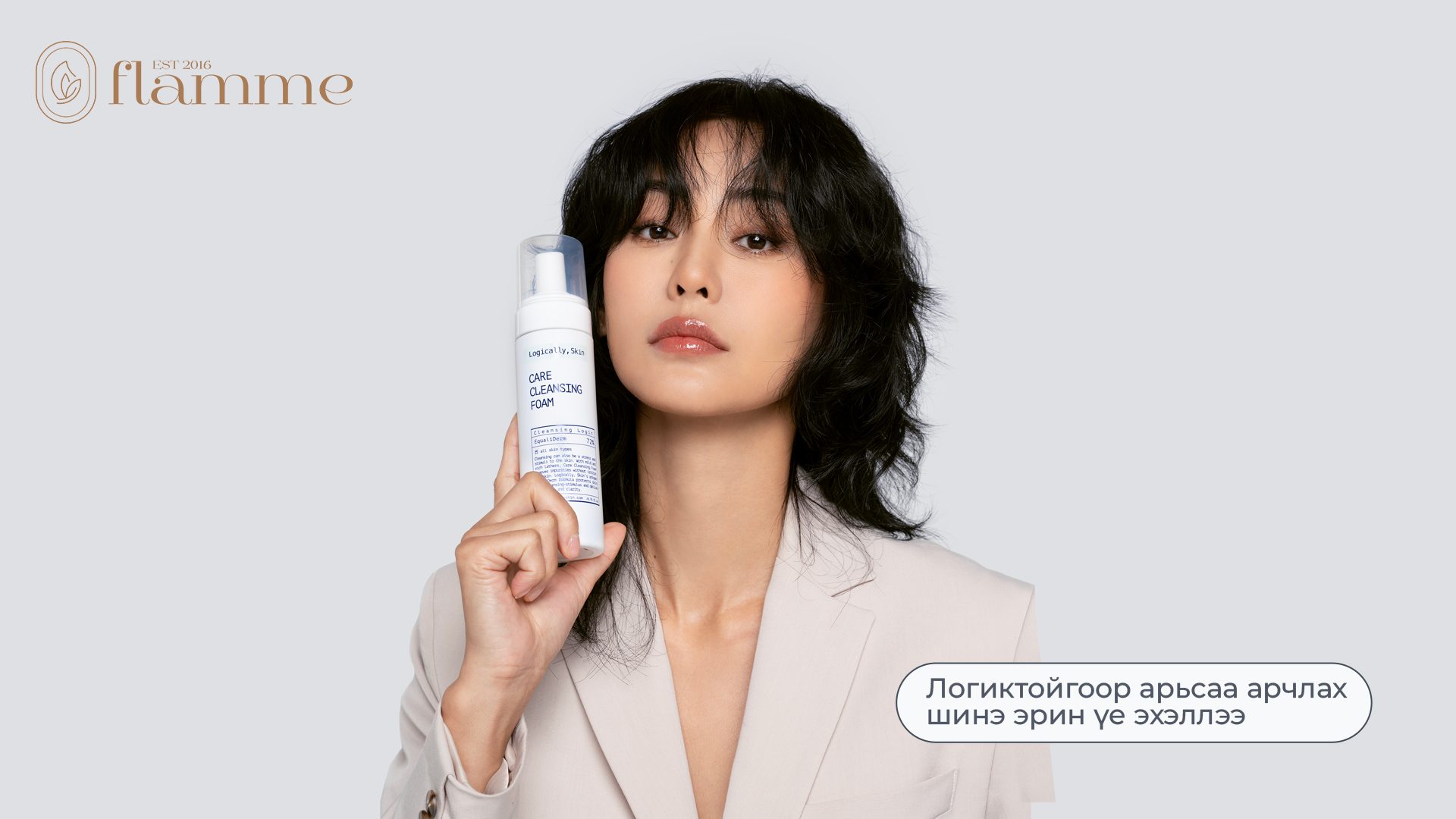 A person with shoulder-length black hair holds up a bottle of One Cleansing Spray. They are wearing a cream-colored blazer. The background is light gray, and there is text in a non-English language on the right side.