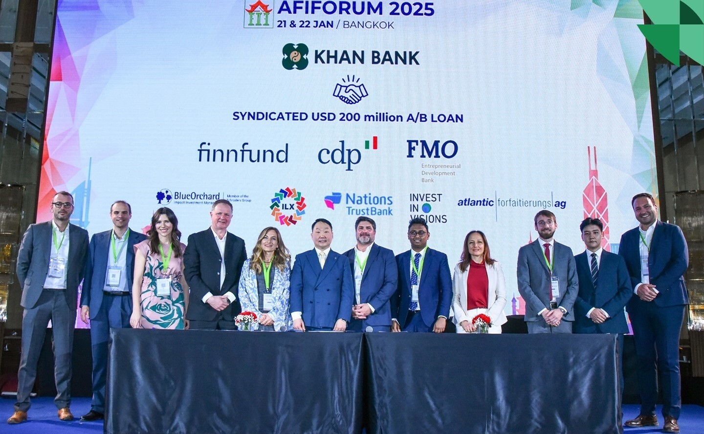 A group of people in formal attire stands on stage at the AIFORUM 2025 in Bangkok. Behind them is a large screen displaying logos of sponsors, including Khan Bank and others. The group smiles for the photo.