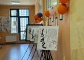 A hallway decorated with colorful balloons on the wall. Several easels display framed calligraphy artworks. Large windows allow natural light into the room, creating a warm and inviting atmosphere.