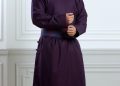 A person wearing a long, dark purple traditional robe stands against a white-paneled wall. The robe features a high collar and a belt. The individual has long, dark hair and is looking confidently at the camera. "Tumen Torgo" is displayed in the image.