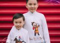 Two children are smiling in front of a red staircase. They are wearing white shirts with colorful, animated character designs. The image features the Tumen Torgo logo and branding.