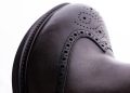 Close-up of a dark brown leather shoe with decorative perforations and stitching. The words "Italian Design" are in the upper left, with a circular logo on the upper right.