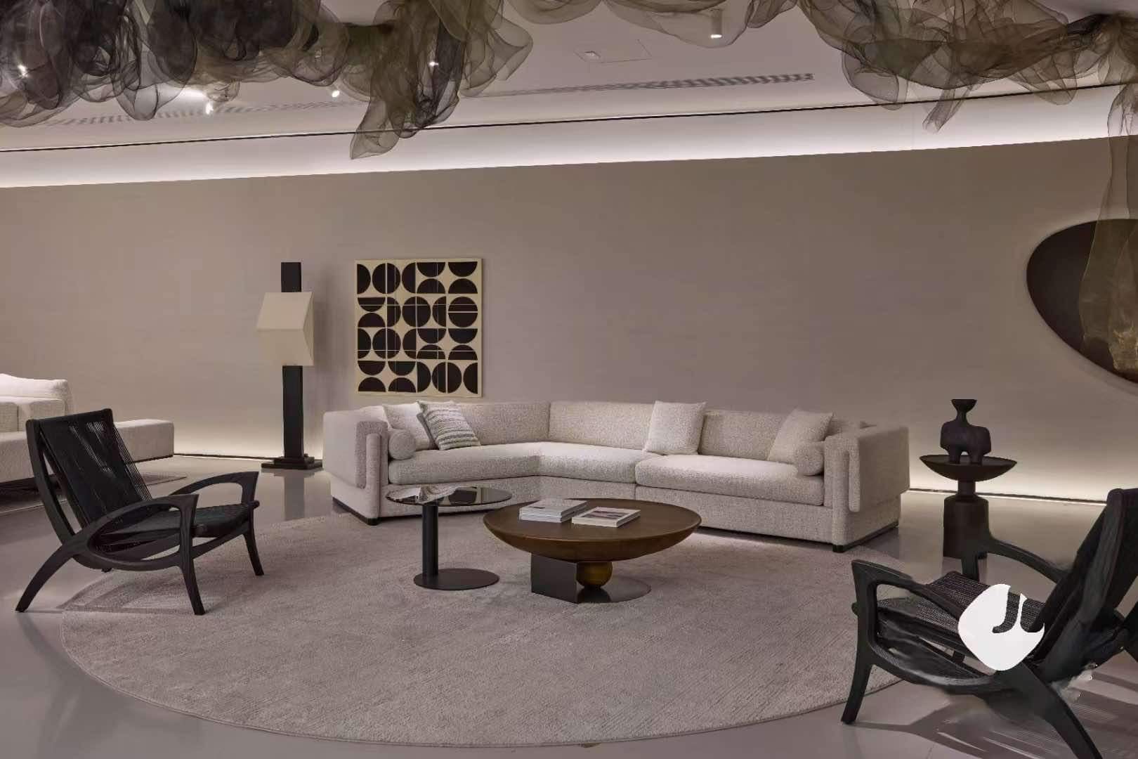 A modern living room with a beige sectional sofa, two black chairs, a round coffee table, large abstract art on the wall, and a neutral rug. Decorative mesh drapes hang from the ceiling. The room is softly lit, creating a cozy ambiance.