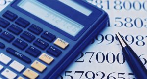 A blue calculator and a pen resting on a sheet filled with large printed numbers. The calculator display is visible, and the pen is positioned alongside, suggesting an active use of both tools for calculations or analysis.