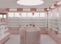 A modern, minimalist skincare store with pastel pink shelving and walls. Central display table holds a few products. Overhead lighting is circular, and large windows allow natural light. Brand names are displayed on signs above shelves.